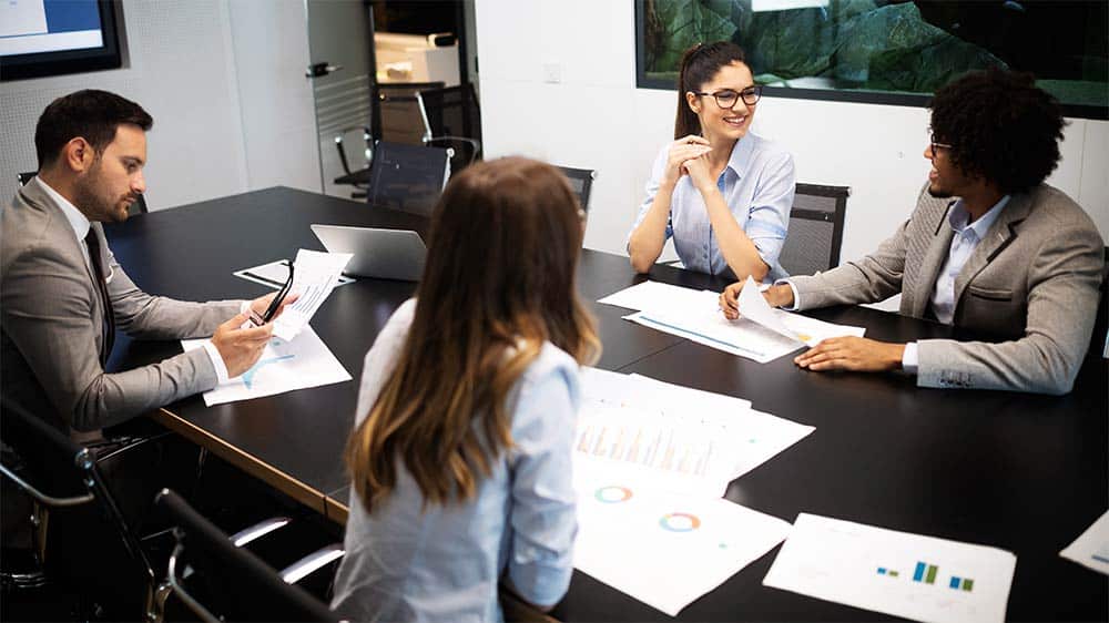 Four people sitting at a conference room table, looking at charts and graphs.