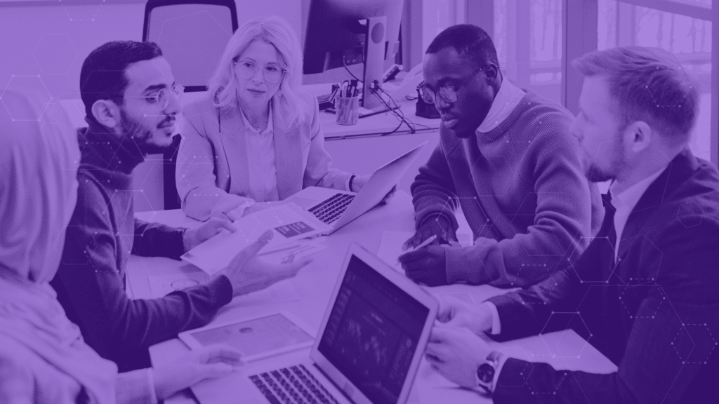 An IT team gathered around a conference table with their laptops open, with a modern purple overlay.